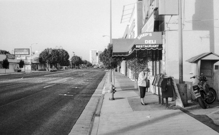 Une femme consulte la presse quotidienne, seule dans une rue de Los Angeles